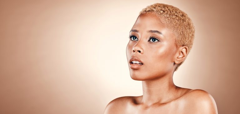 Femme avec une coupe très courte et des cheveux blonds dorés, mise en valeur par un portrait lumineux sur fond beige