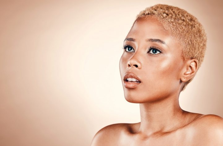 Femme avec une coupe très courte et des cheveux blonds dorés, mise en valeur par un portrait lumineux sur fond beige