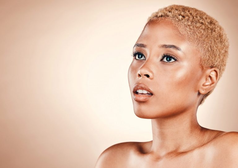 Femme avec une coupe très courte et des cheveux blonds dorés, mise en valeur par un portrait lumineux sur fond beige